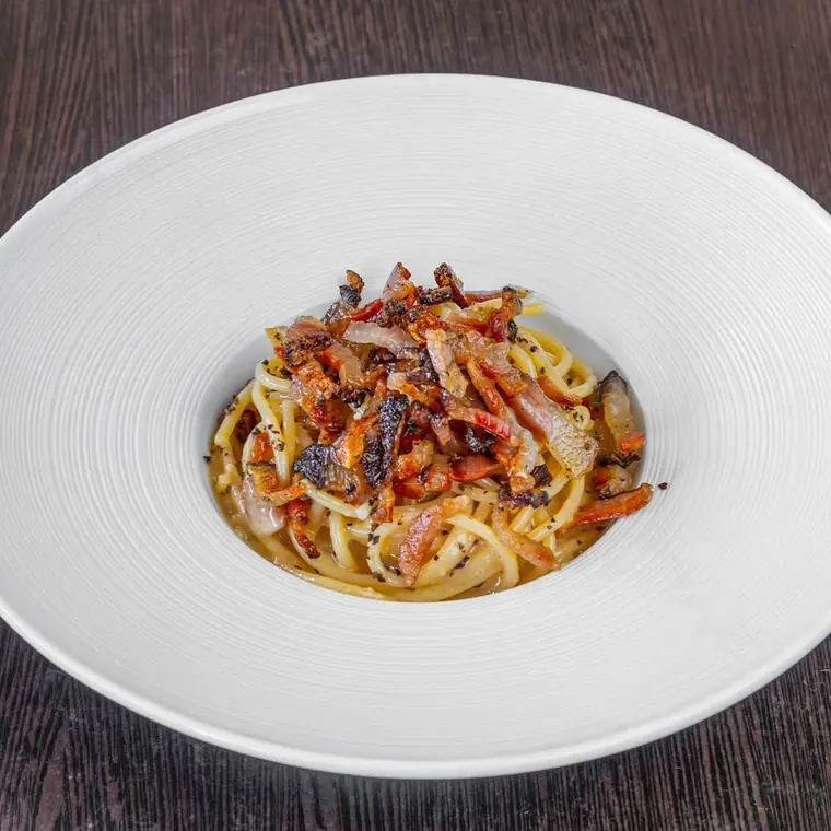 Spaghetti with guanciale served in a wide white bowl